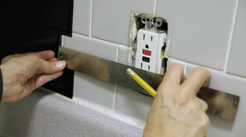 A person measuring a wall outlet Description automatically generated