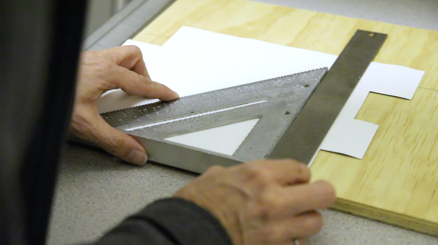 A person using a square to measure a piece of paper Description automatically generated